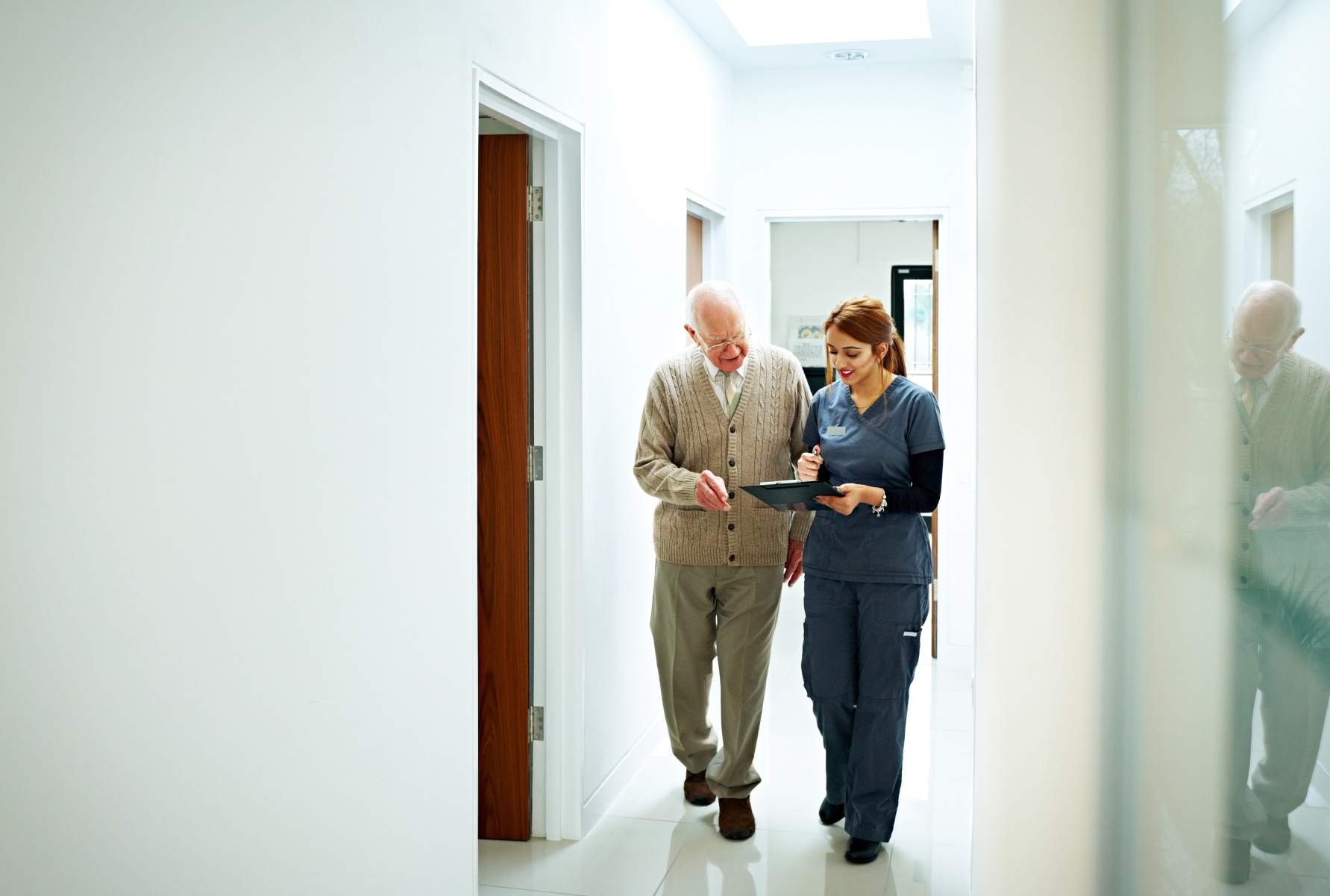 Leva med KOL, äldre man går tillsammans med sjukvårdspersonal genom korridor